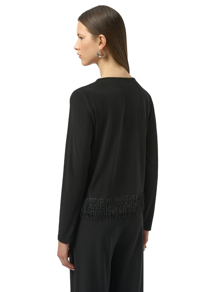 Person wearing a black long-sleeve top with fringe detail at the bottom and matching black pants, facing sideways.