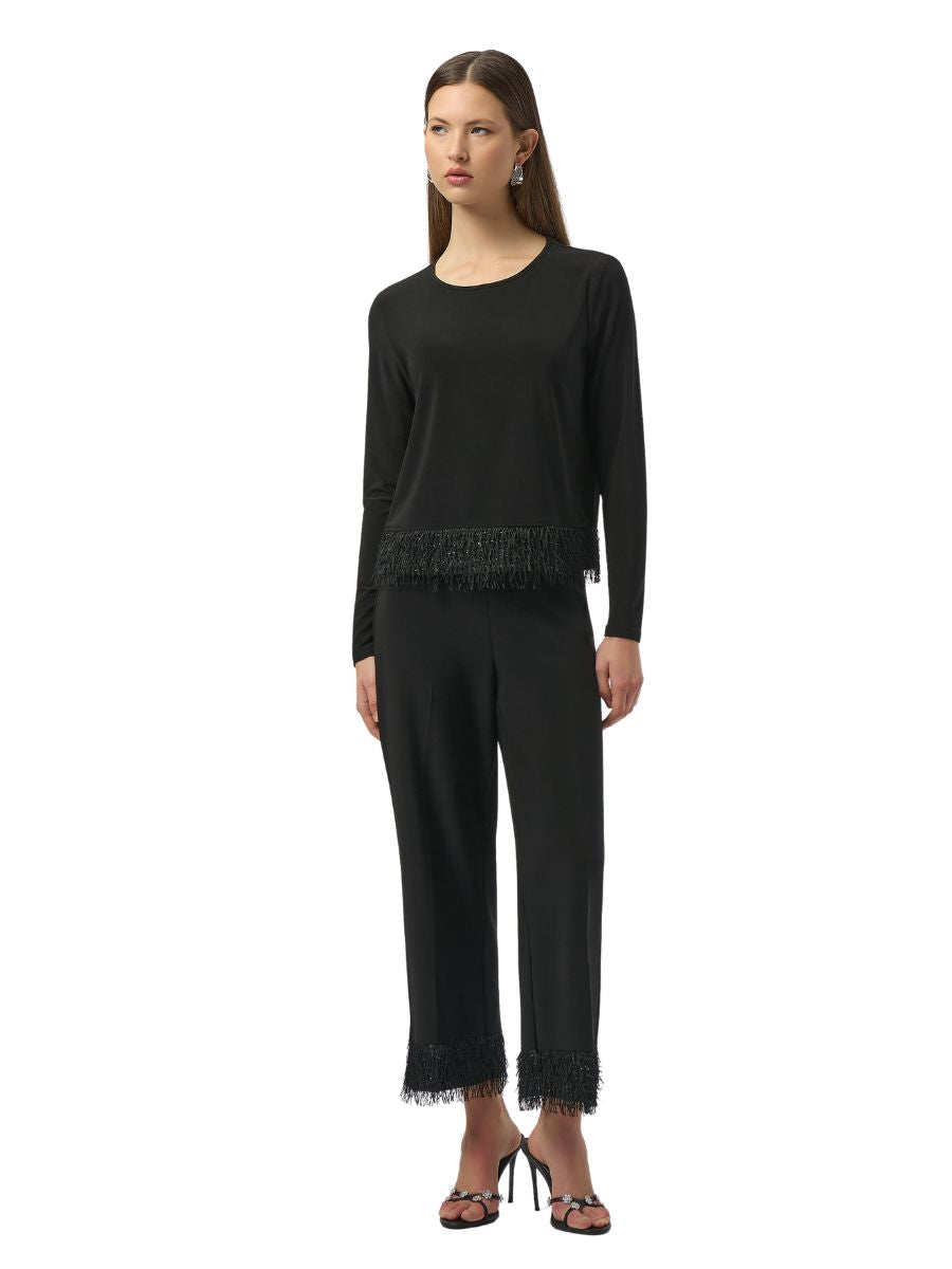 Black long-sleeve top and pants with fringed trim detail worn with black high-heeled sandals against white background