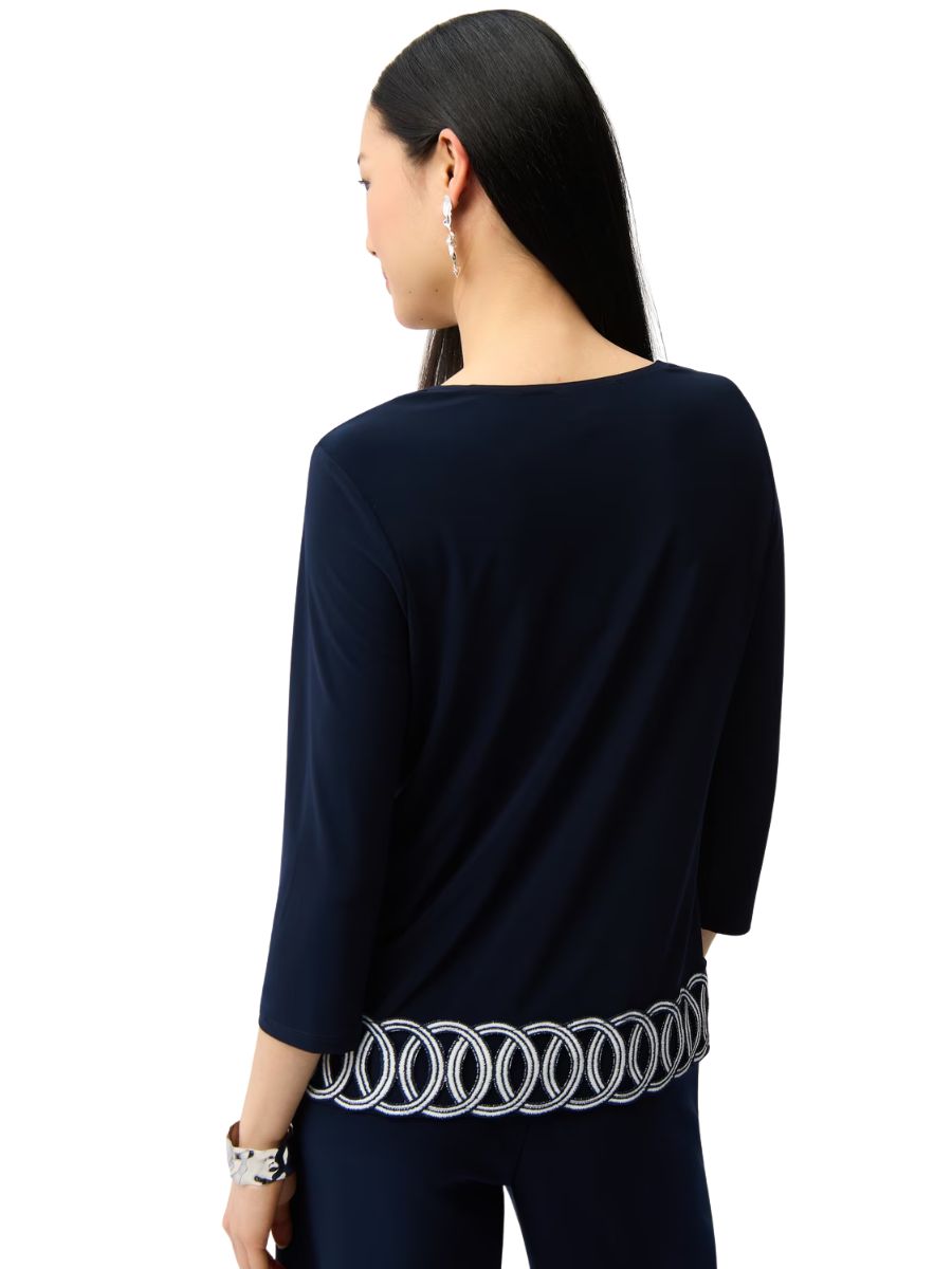 Navy long-sleeve top with white embroidered circular pattern along the hem worn by a person with long dark hair