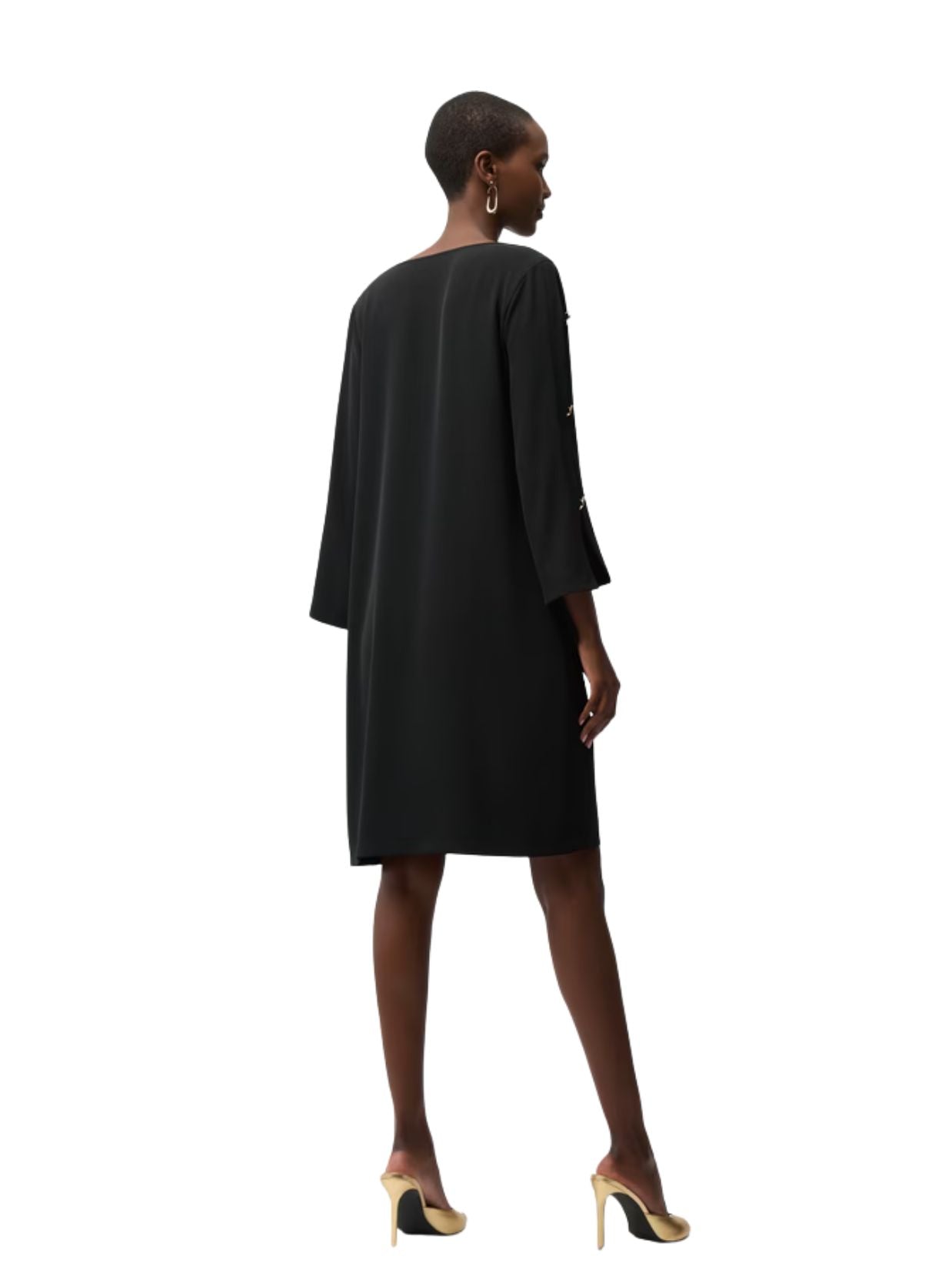 Back view of a person wearing a loose black long-sleeve dress paired with beige and black high-heeled shoes.