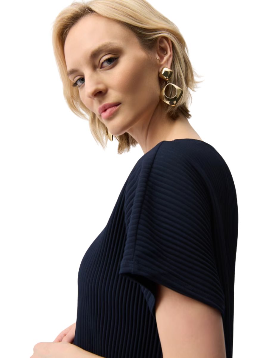 Person with short blonde hair wearing large gold statement earrings and a navy ribbed textured top