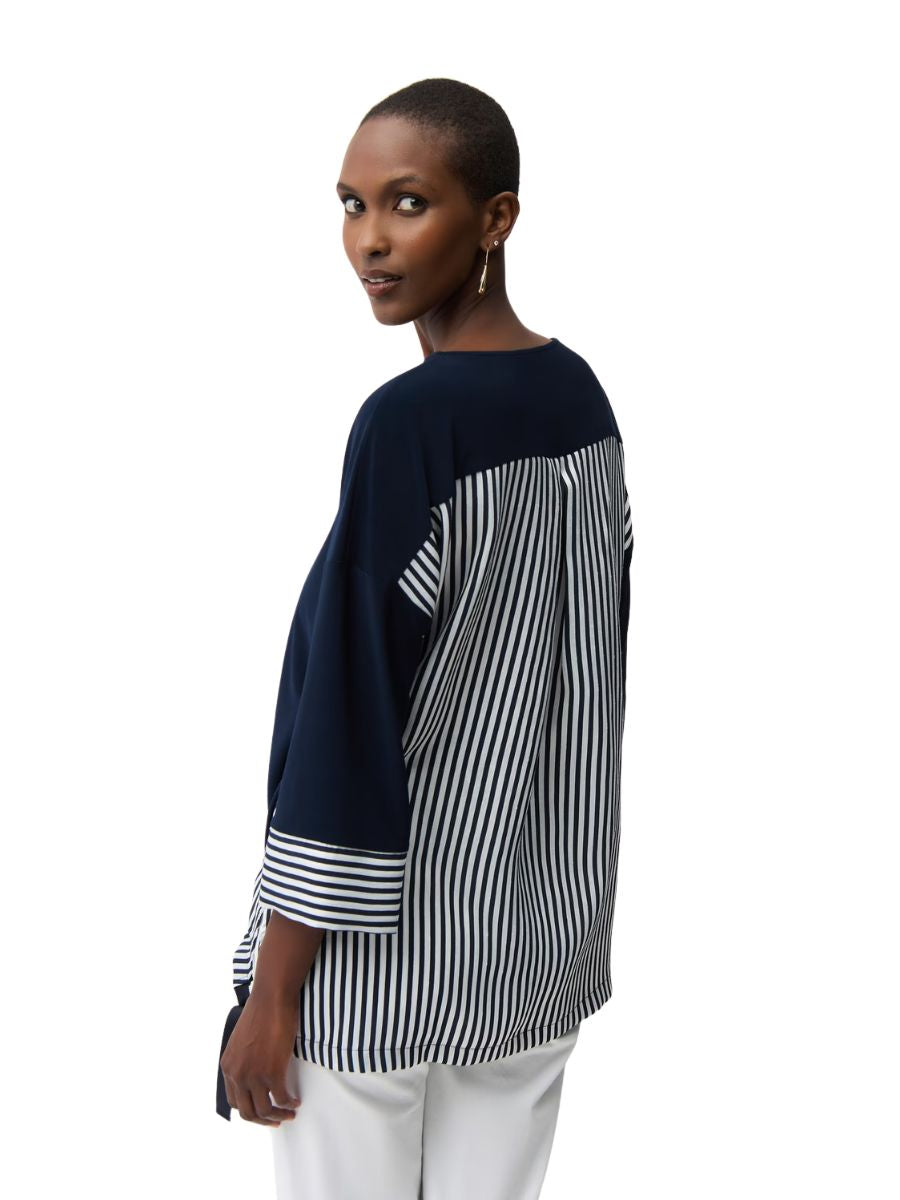 Person wearing a navy and white striped long-sleeve top paired with white pants against a white background
