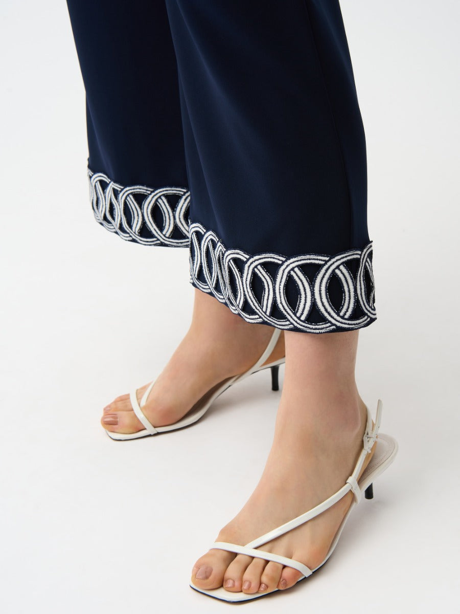 Close-up of navy pants with white circular embroidery on hems paired with white strappy low heel sandals, Joseph Ribkoff Suit and Tache 26" Crop Pant