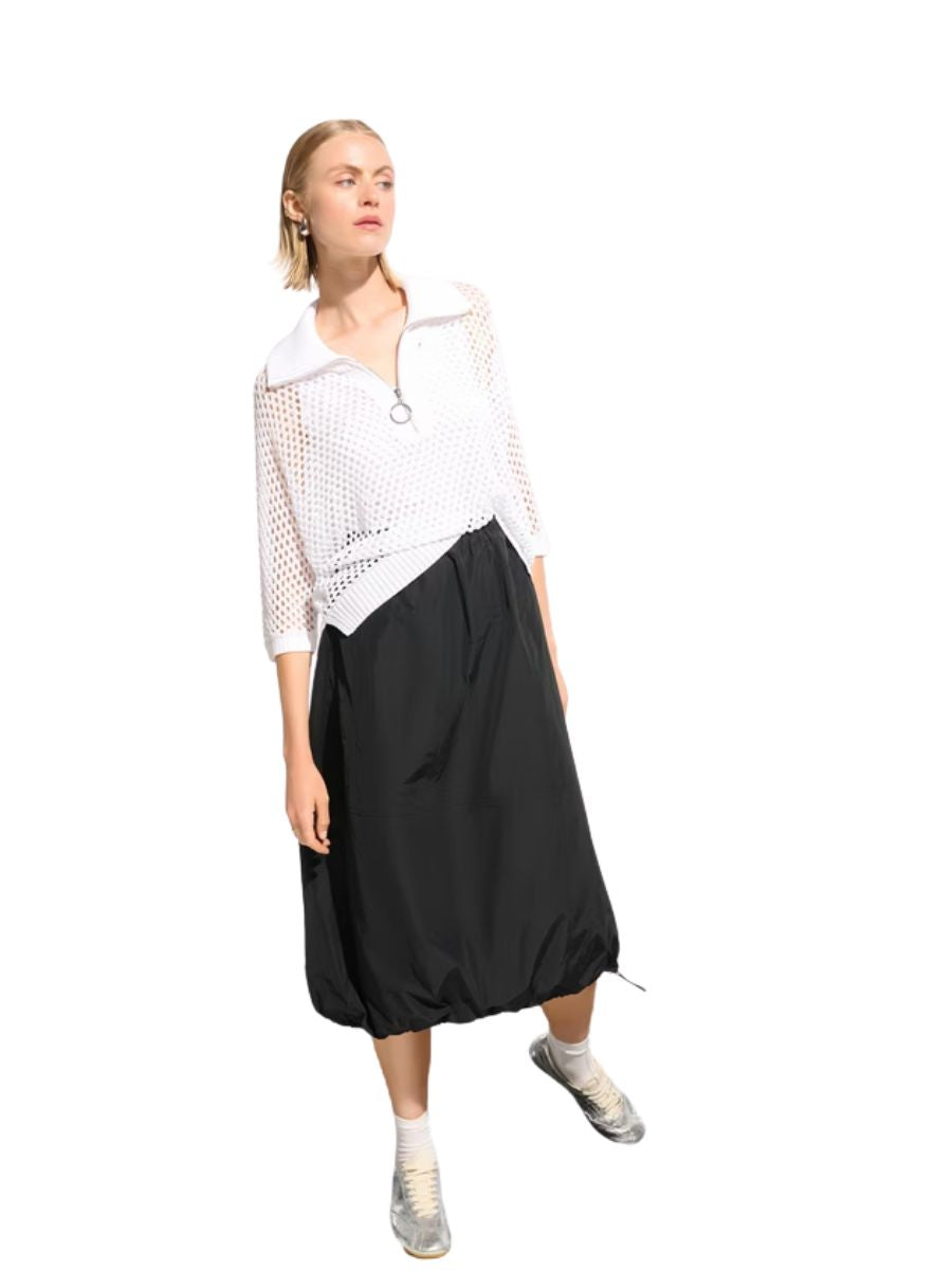 Slim figure in white mesh sweater with zipper and black midi skirt paired with white sneakers on white background