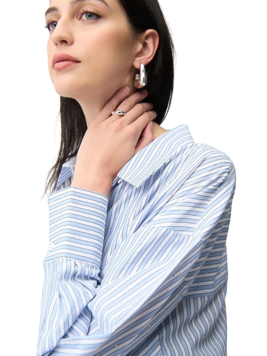 Close-up of person in blue and white striped shirt wearing silver hoop earrings and a silver ring on the hand near the neck
