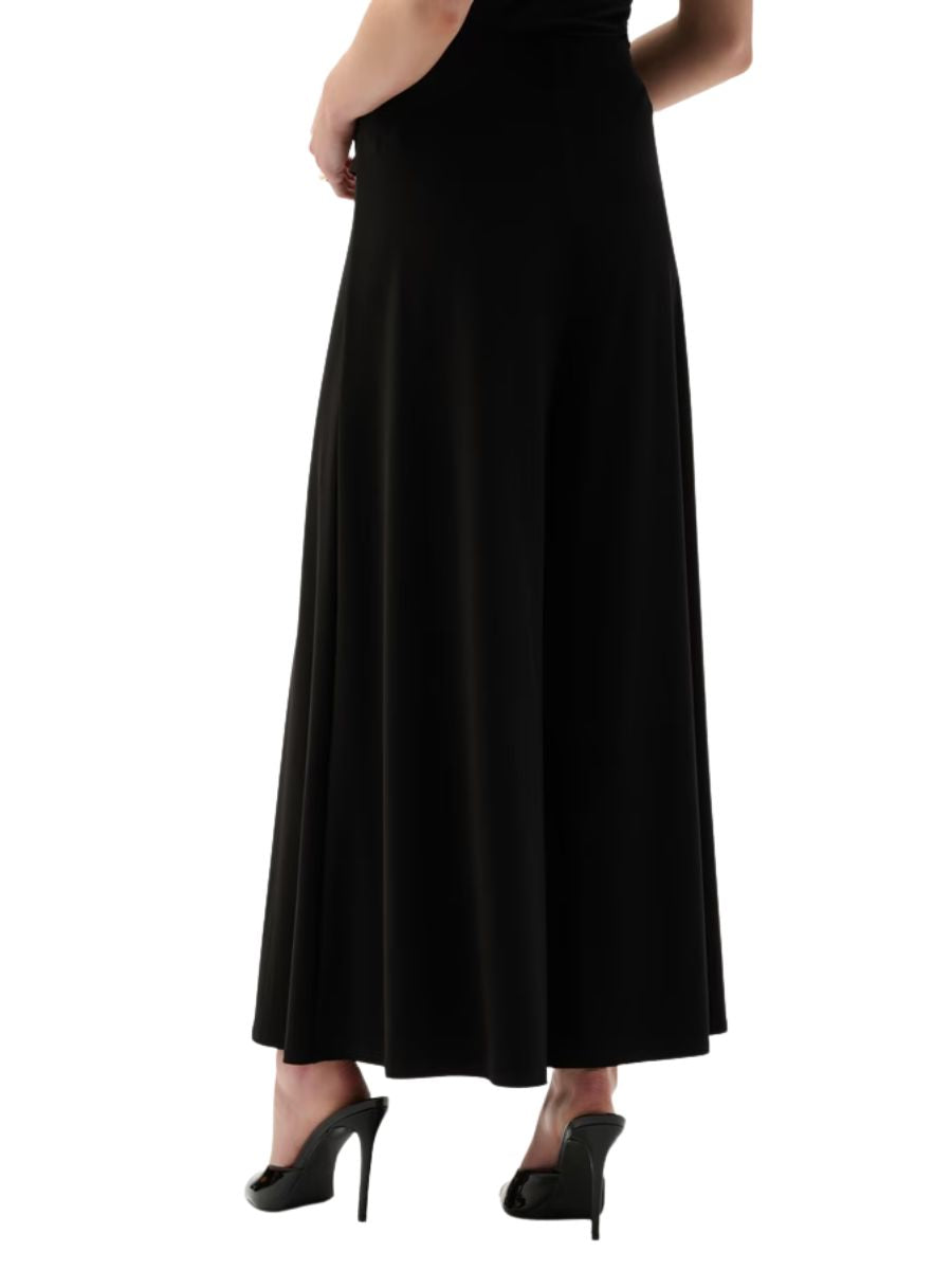 Back view of a long black skirt paired with black high-heeled shoes on a white background