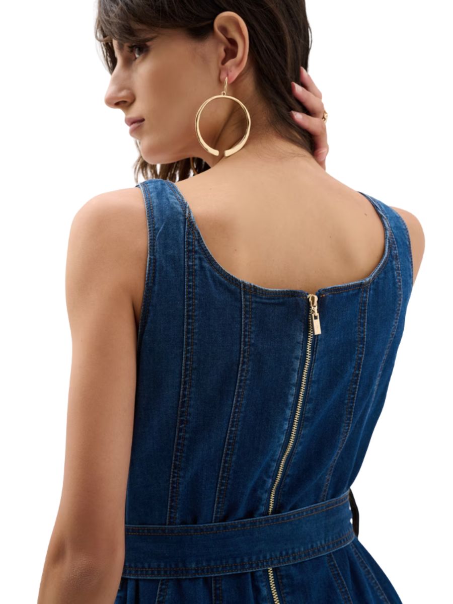 Back view of a sleeveless dark denim garment with a visible gold zipper and large circular gold earrings.