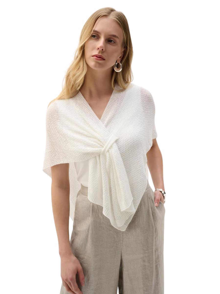 Person wearing a textured white knit shawl over a white top and beige high-waisted pants with hand in pocket.