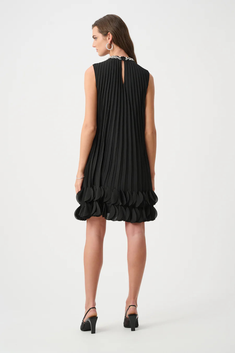 Sleeveless black pleated dress with layered circular hem detail, paired with black heeled sandals and hoop earrings.