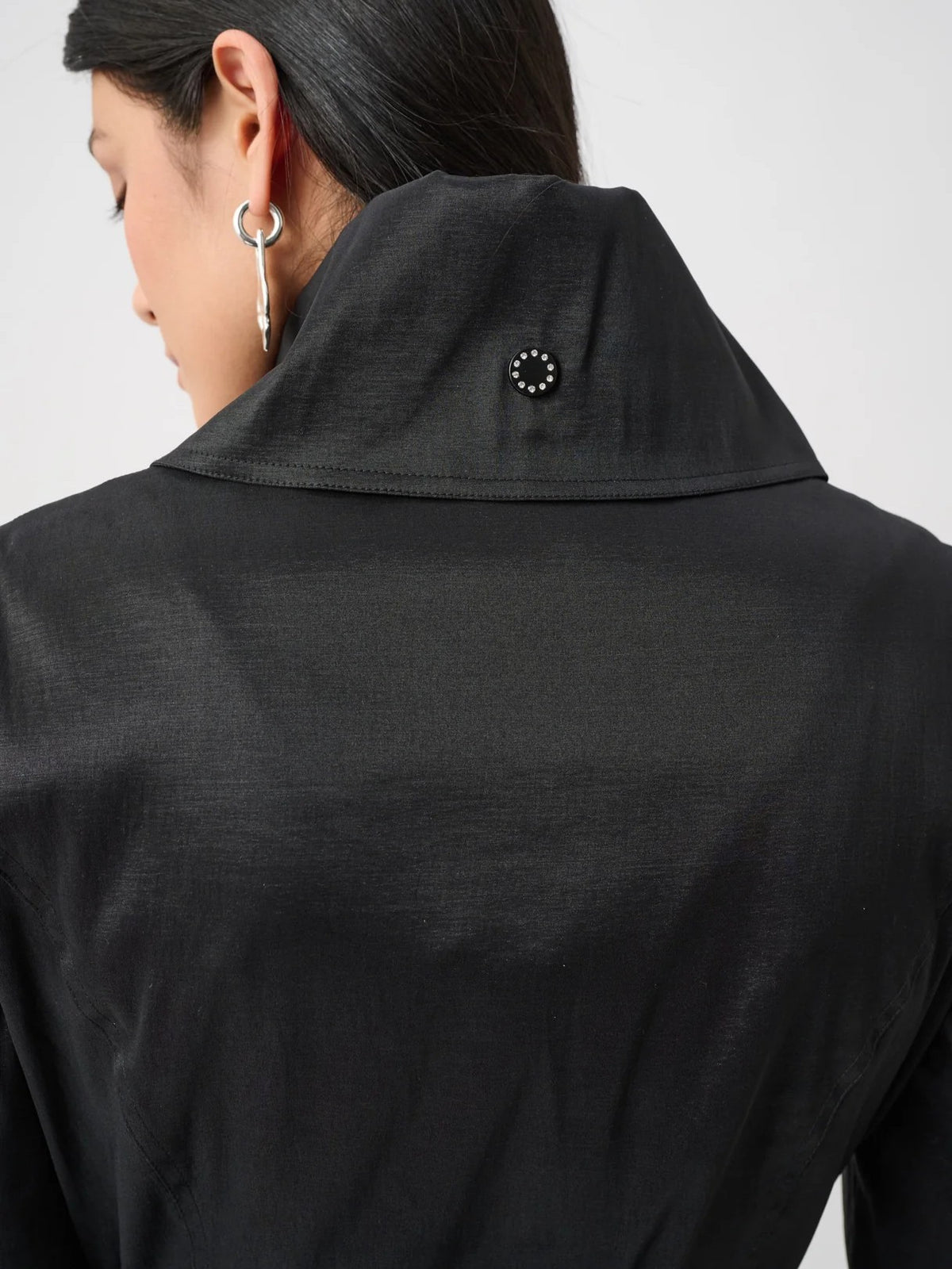 Close-up of a black jacket collar with a round stud detail on the back, and part of an ear with a silver earring visible.