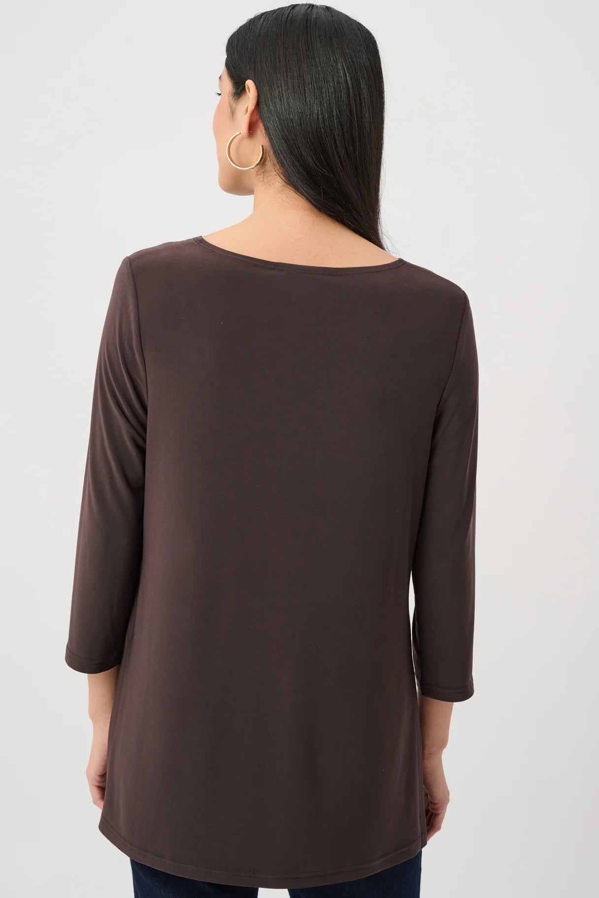 Back view of a person with long dark hair wearing a mocha-colored long sleeve top and hoop earrings