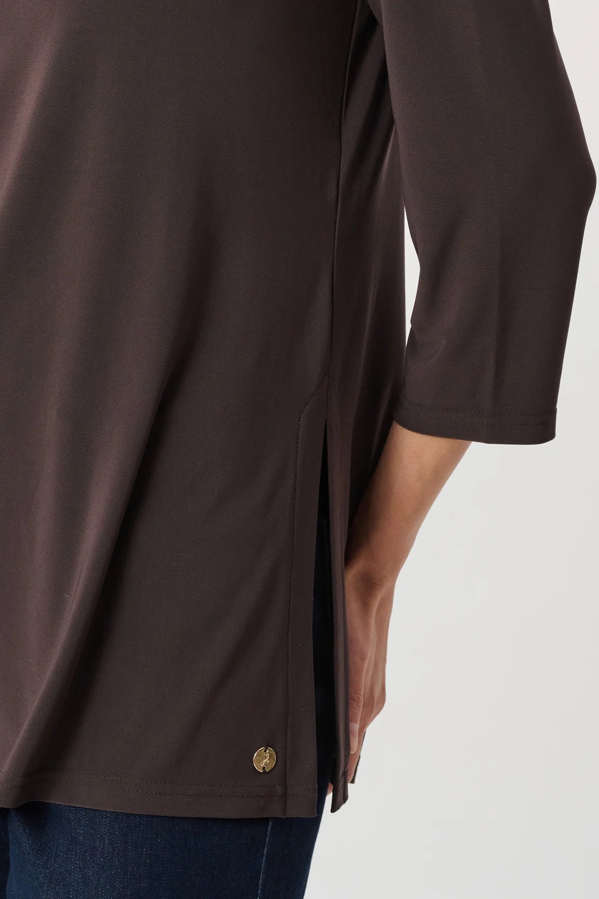Close-up of a mocha-colored top with three-quarter sleeves and a small side slit showing part of dark denim pants.