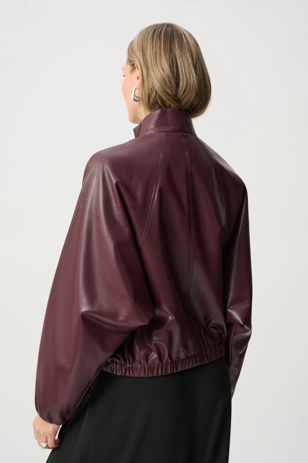Back view of a burgundy faux leather jacket with gathered elastic hem and high collar against a plain background.