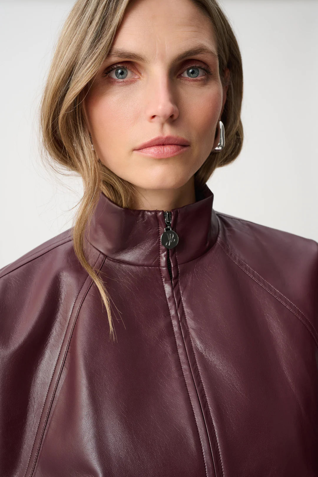 Close-up of a high-neck burgundy leather jacket with a front zipper and silver geometric earrings visible.