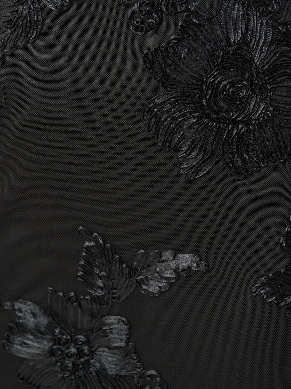 Black fabric with textured floral embroidery in a raised, glossy finish creating a detailed pattern.