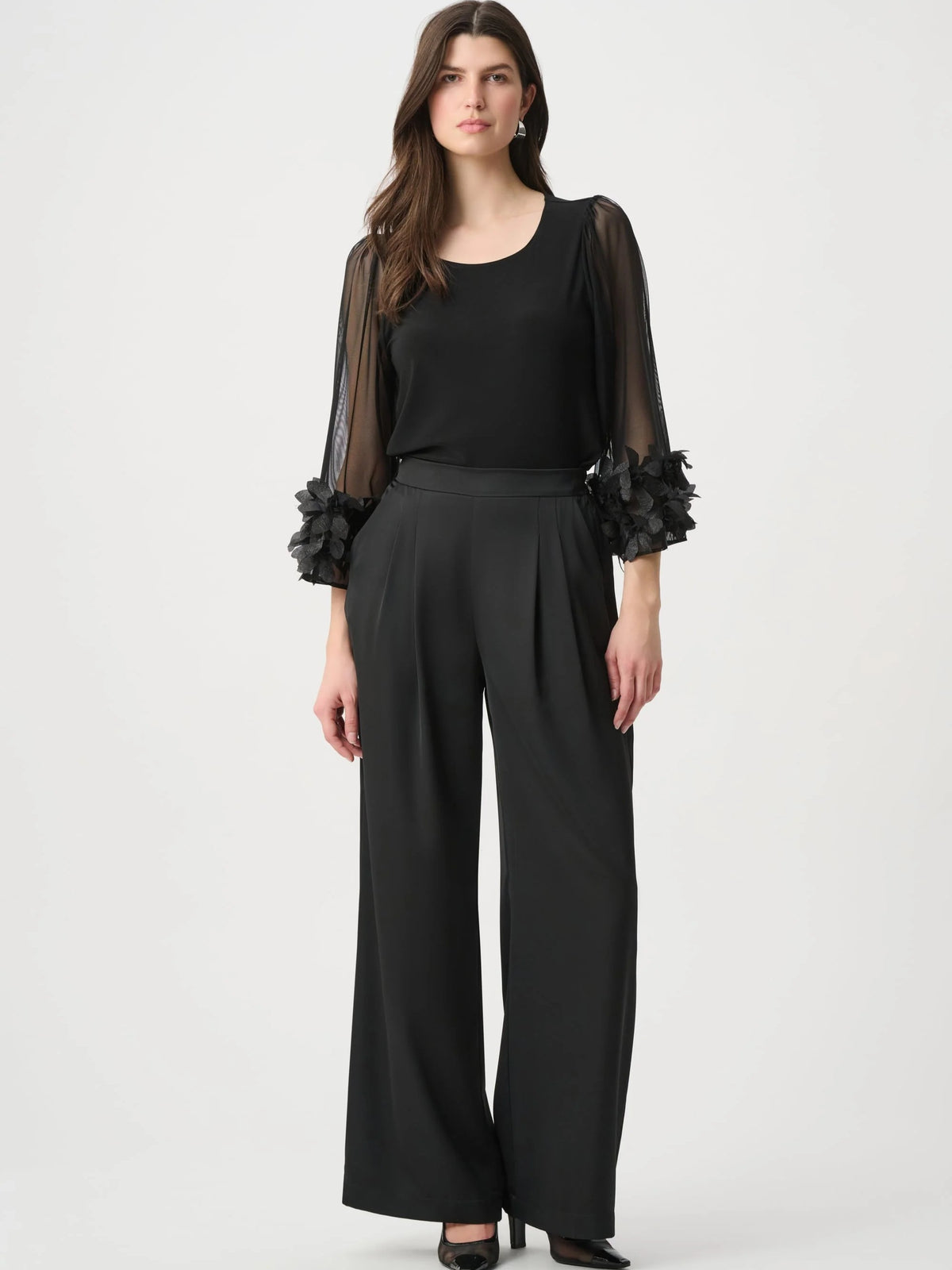 Black top with sheer puffed sleeves and floral cuffs paired with wide-leg black trousers and black heels.