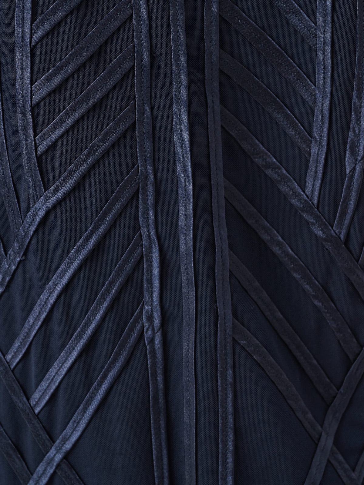 Close-up of dark fabric with textured vertical and diagonal velvet strips forming a geometric pattern on outerwear.