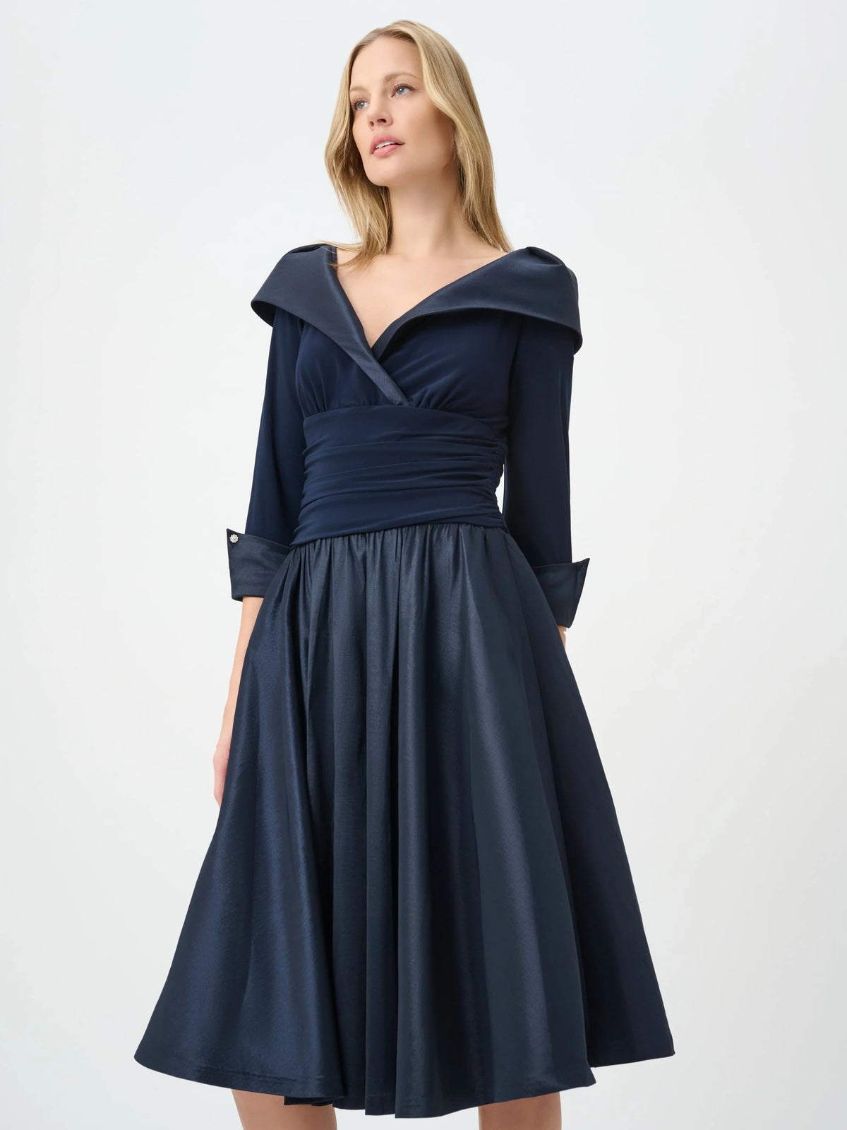 Model in a navy off-shoulder dress with three-quarter sleeves and a gathered waist detail against a white background.