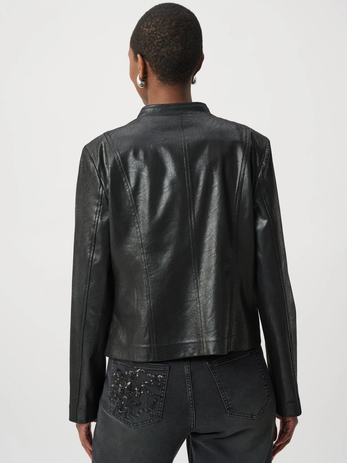Back view of a short black leather jacket paired with dark jeans featuring decorative embroidery on the pocket.