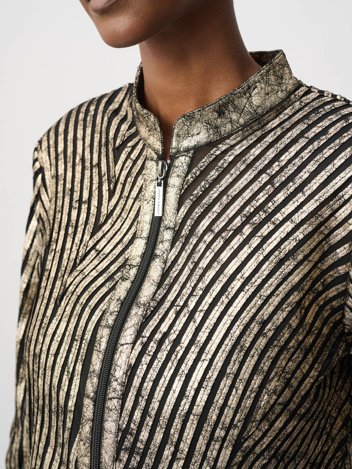 Close-up of a metallic gold and black striped jacket with a front zipper and high collar.