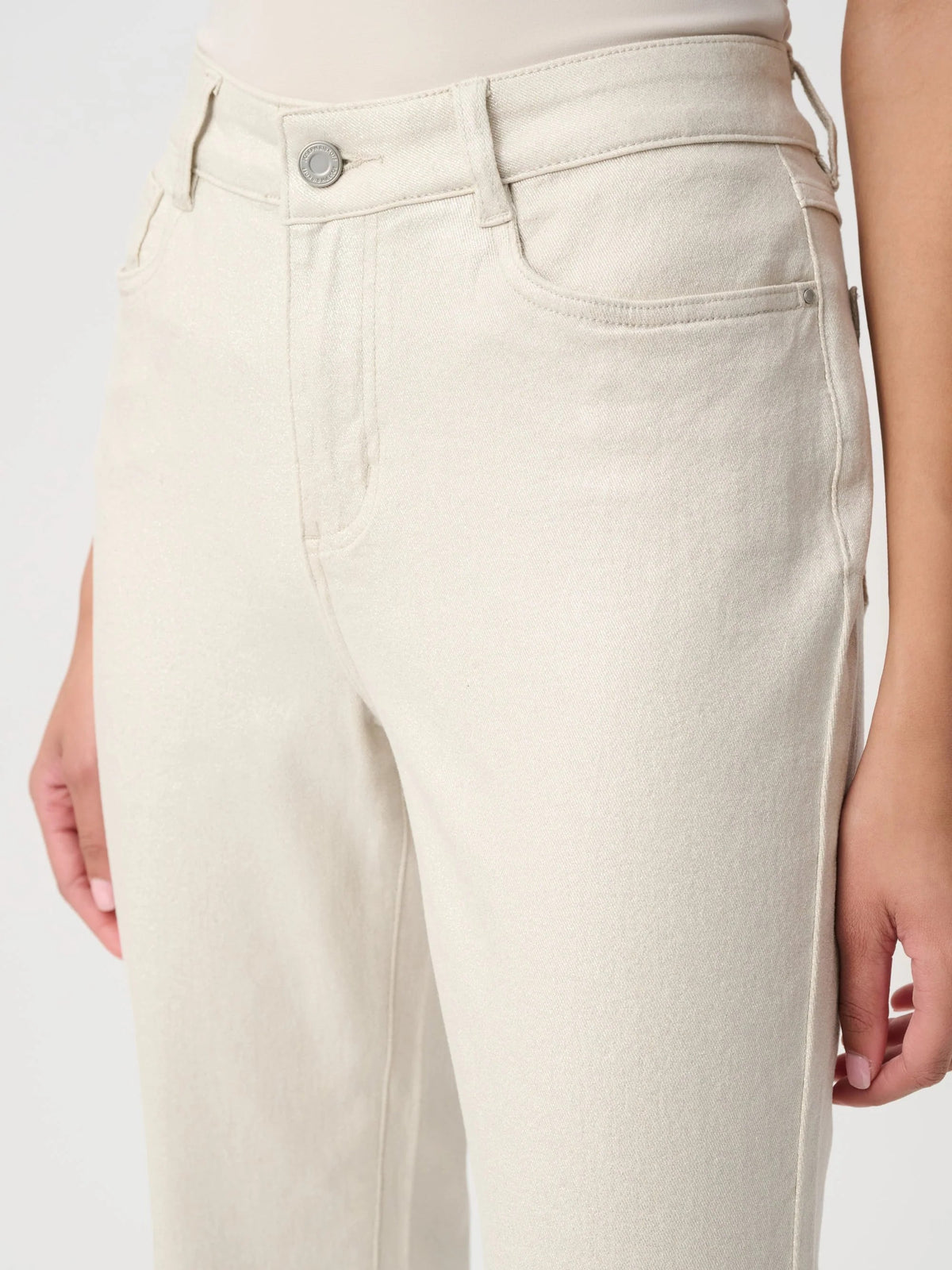 Close-up of light beige denim jeans with front pockets and a metal button closure on a neutral background.
