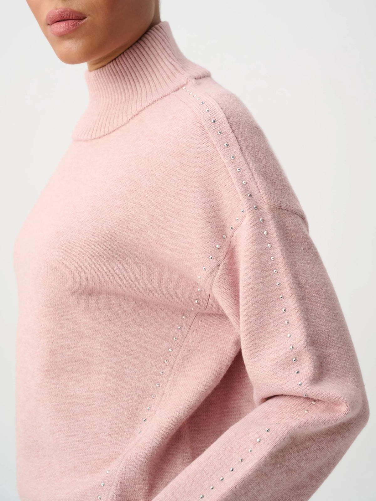 Close-up of pink turtleneck sweater with small metallic stud details along the shoulder and sleeve seams