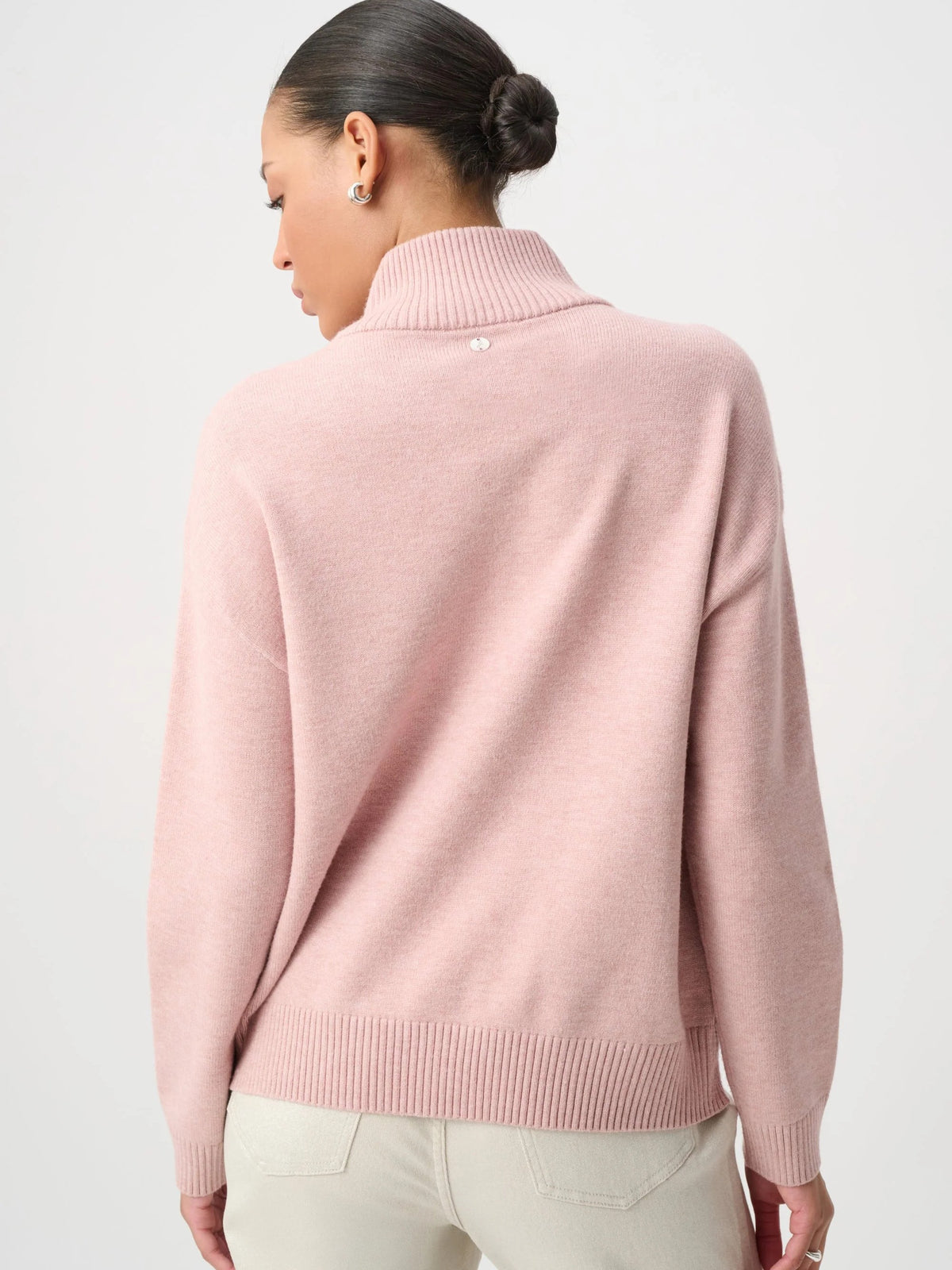 Back view of a soft pink turtleneck sweater paired with light beige pants against a plain background.