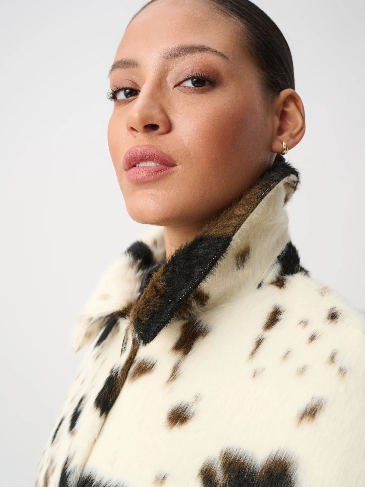 Close-up of a face with neutral expression and a faux fur coat with a spotted pattern and high collar.