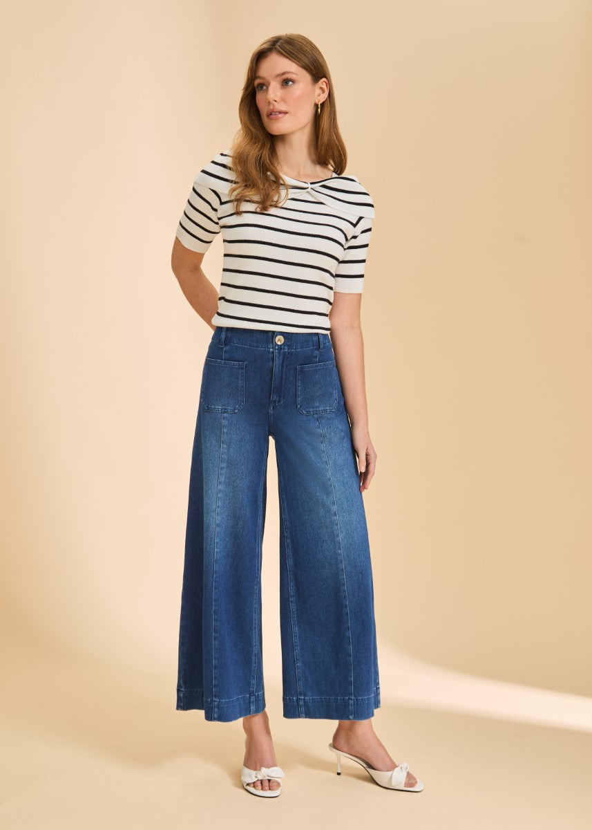 Person in a striped short-sleeve top and wide-leg denim pants standing on a beige background