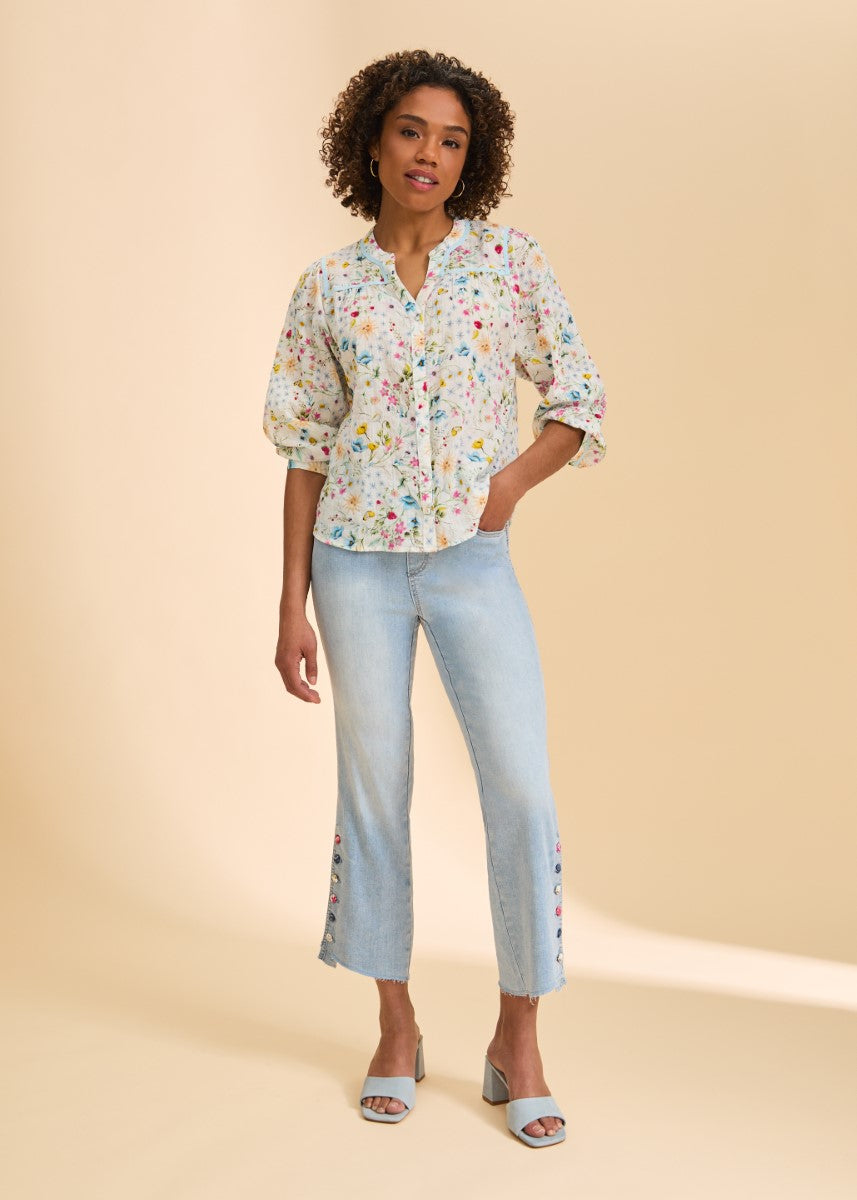 Curly-haired person in floral blouse, light blue cropped jeans with side buttons, and light blue heeled sandals.