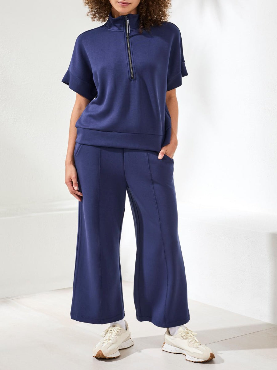 Person dressed in navy blue wide-leg pants and short-sleeve top with a front zipper, paired with white sneakers.