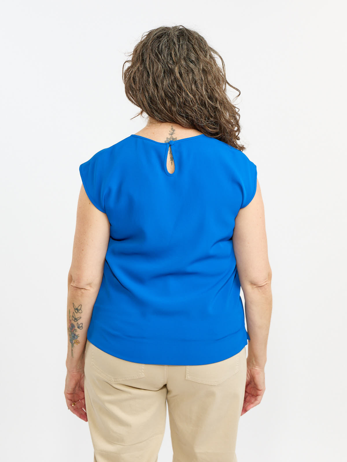 Blue short sleeve blouse with a keyhole back closure, paired with beige pants against a white background.