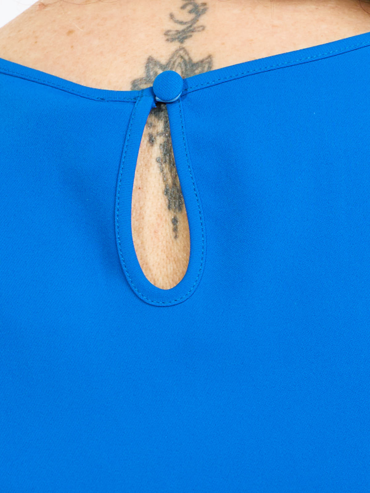 Close-up of a blue top’s back neckline featuring a covered button and keyhole opening with visible tattooed skin beneath.