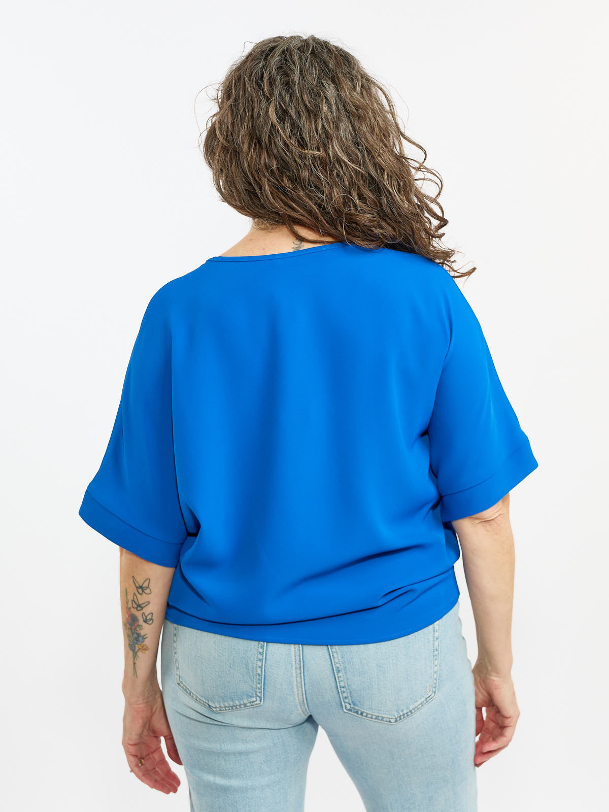 Blue short-sleeve top paired with light blue denim jeans, viewed from the back on a white background.
