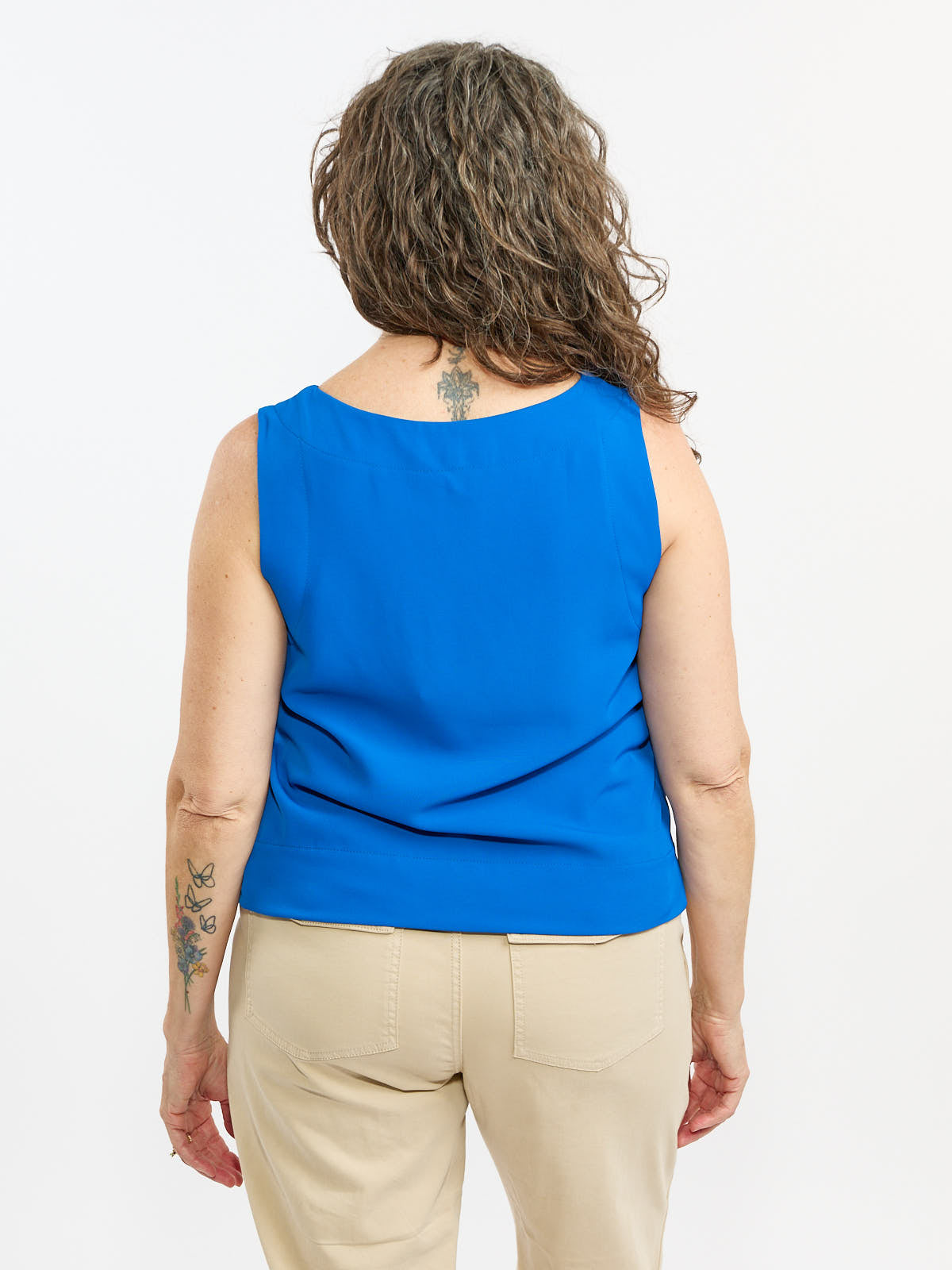 Back view of a sleeveless royal blue top paired with beige pants on a person with curly hair and visible tattoos.