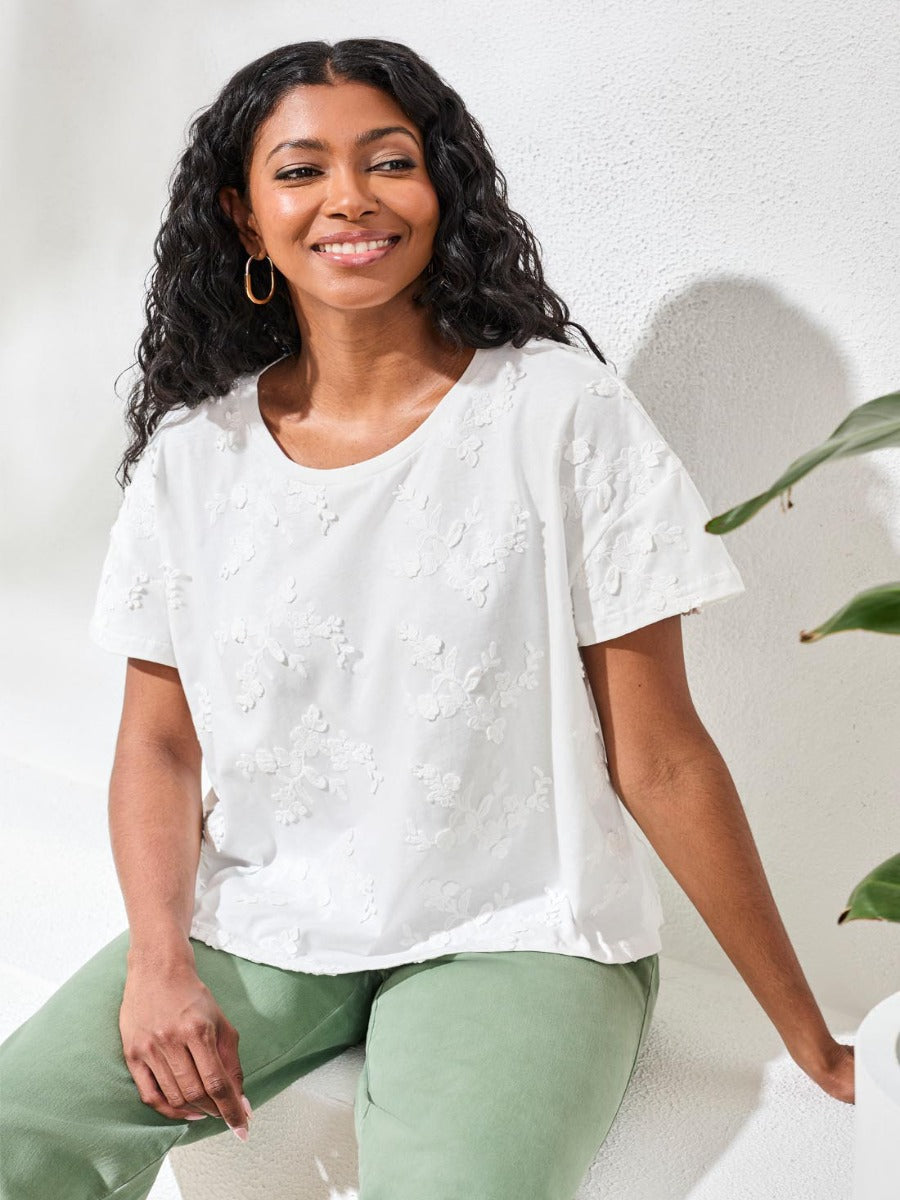 Smiling model seated wearing Tribal Boho Bloom Embroidered Cotton Short Sleeve Top by Tribal Sportswear Inc.