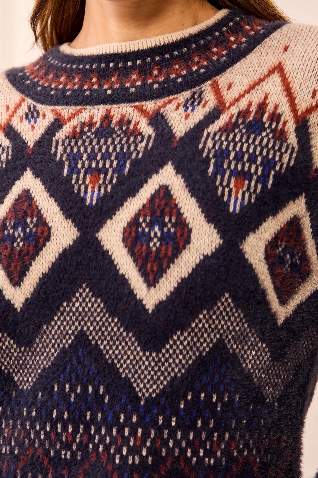 Close-up of a knitted sweater with geometric patterns in navy, cream, rust, and blue colors.