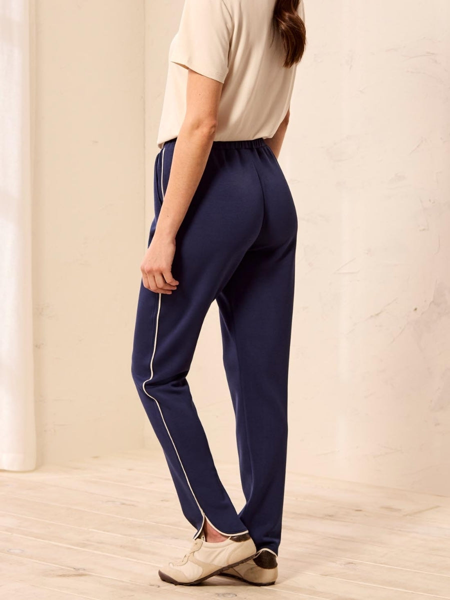 Navy blue pants with white side stripes and ankle slits paired with beige short-sleeve top and sneakers.