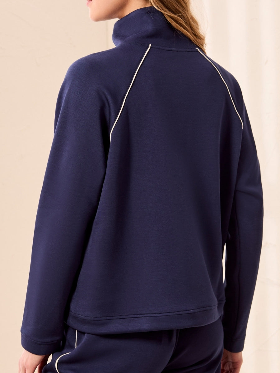 Back view of navy blue long-sleeve top with white piping detail along raglan seams and high collar.