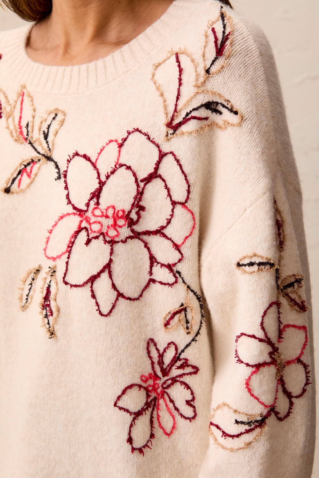 Cream sweater with red and brown floral embroidery on the chest and sleeve, featuring a ribbed neckline