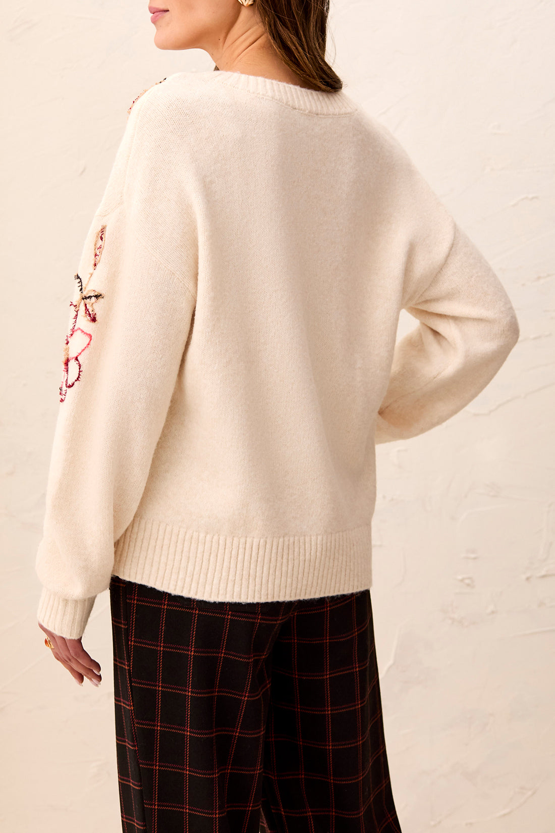 Cream-colored sweater with ribbed hem and cuffs paired with dark plaid pants against a neutral background