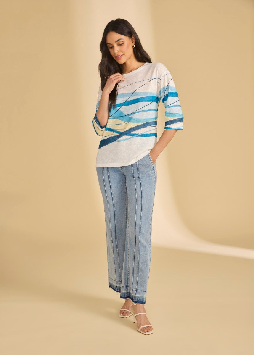 Person wearing a white and blue abstract patterned top with light blue wide-leg denim jeans and white heels.