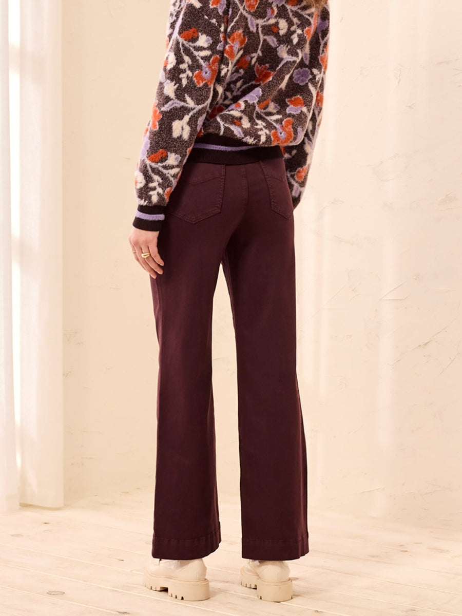 Back view of burgundy wide-leg pants paired with floral patterned sweater and beige boots on wooden floor.
