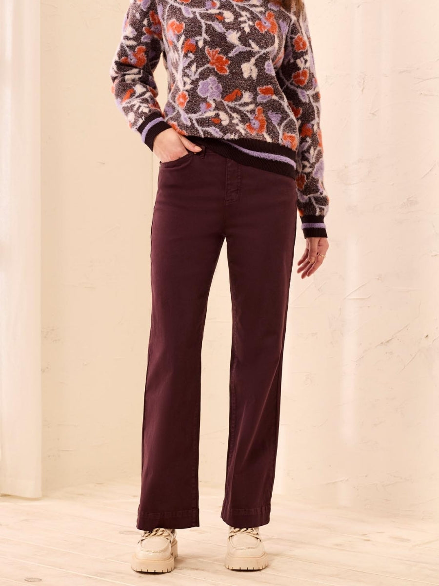 Straight-leg dark brown pants paired with a floral patterned sweater and beige shoes on a light background.