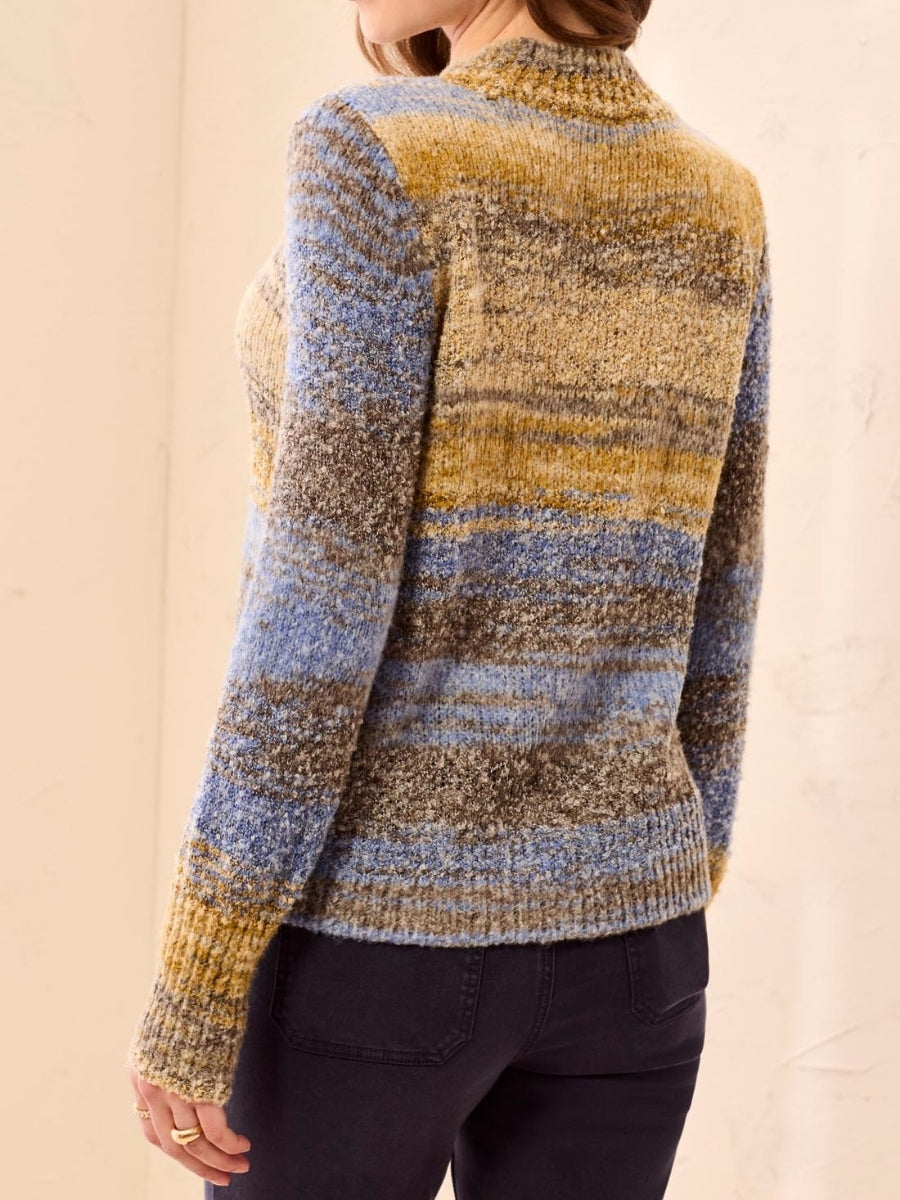 Back view of a multi-colored knit sweater with blue, mustard, and brown stripes paired with dark pants.