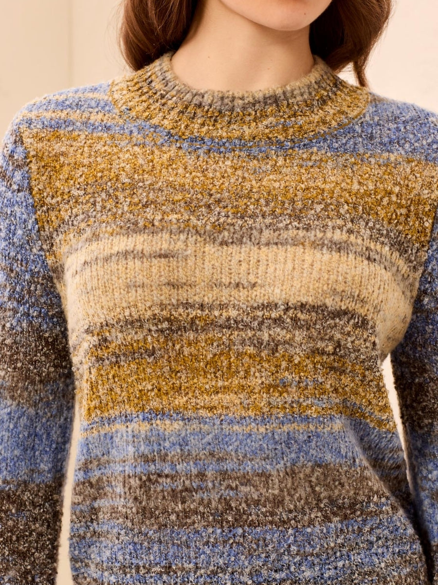 Close-up of a soft textured sweater with horizontal stripes in shades of blue, beige, mustard, and gray.