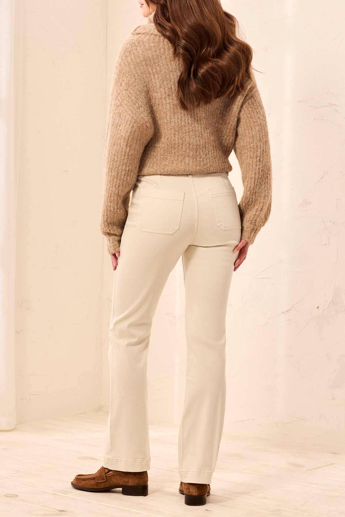Back view of a beige knit sweater paired with off-white straight-leg pants and brown loafers.