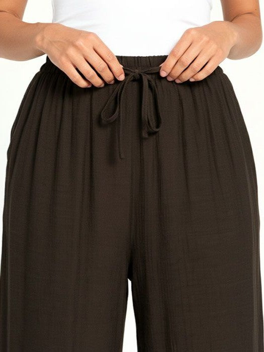 Close-up of hands tying the drawstring on black wide-leg pants made of textured fabric.