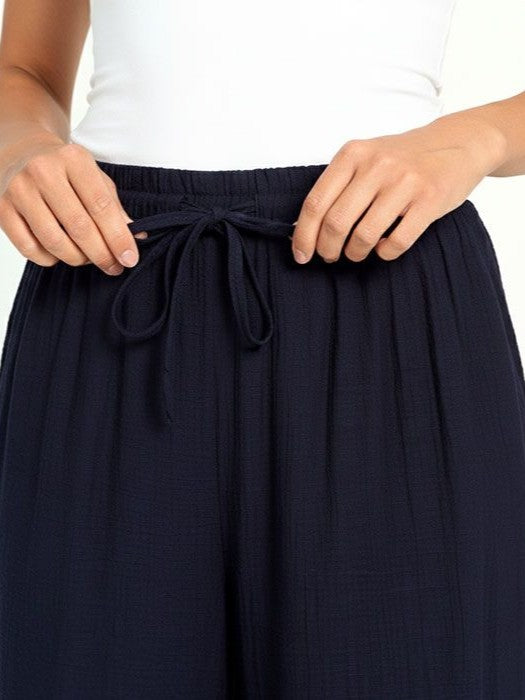 Hands adjusting the drawstring on navy blue textured fabric pants paired with a white top.
