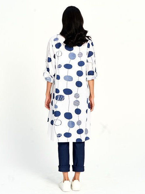 Long white coat with blue circular patterns paired with dark rolled-up pants and white shoes, viewed from the back.